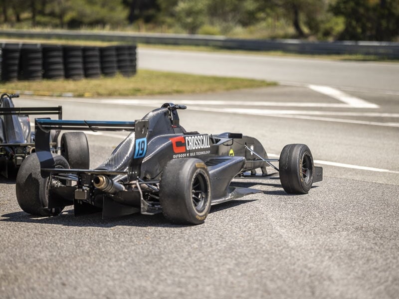 Vue arrière d'une Formule Renault noire numéro 19 sur piste avec barrières et arbres en arrière-plan.