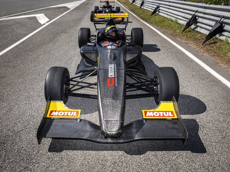 Formule Renault noire vue de face avec autocollants Motul sur piste et autres voitures en arrière-plan.