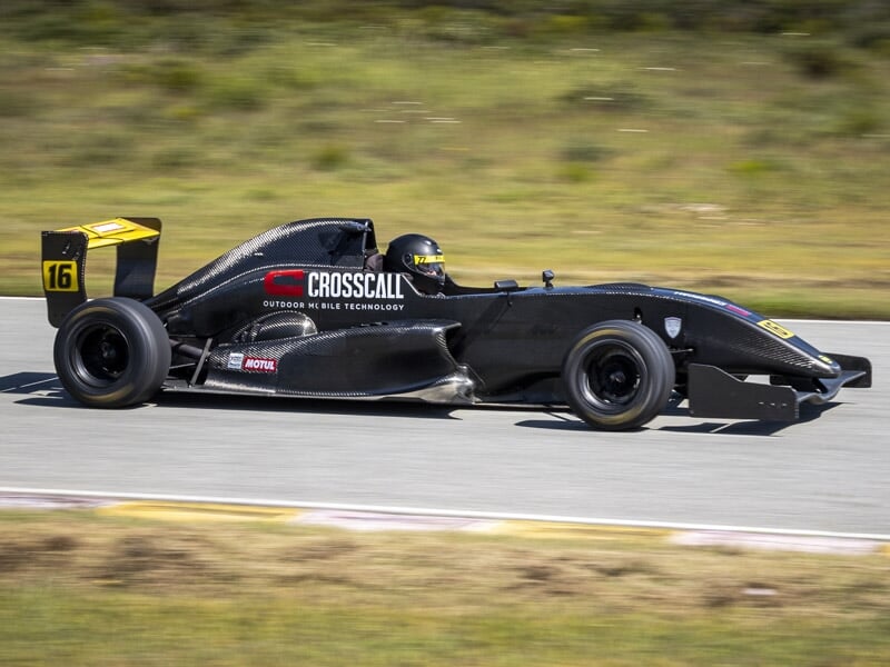 Formule Renault noire numéro 16 en virage sur piste avec pilote casqué et décor naturel flou.