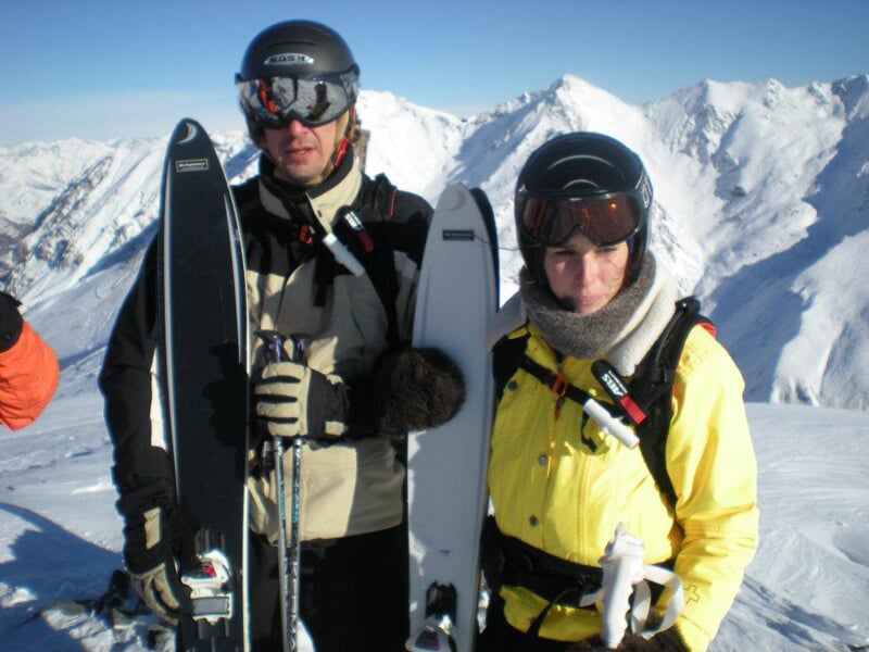 Deux skieurs en tenue d'hiver posant avec leurs skis devant un paysage montagneux enneigé.