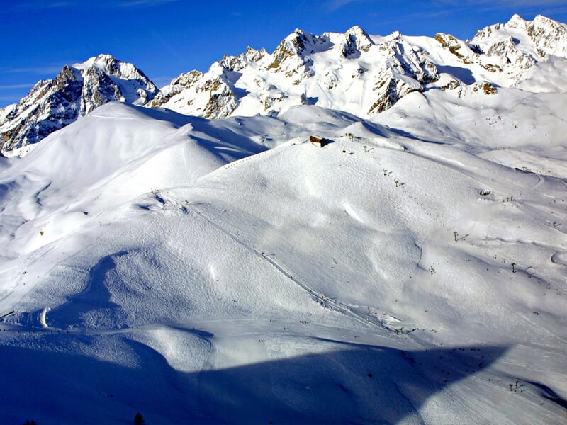 Vue panoramique de montagnes enneigées avec un ciel bleu et des sommets rocheux en arrière-plan.