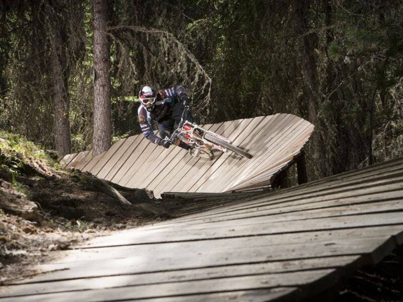 VTTiste en tenue complète prenant un virage serré sur une piste en bois dans une forêt.