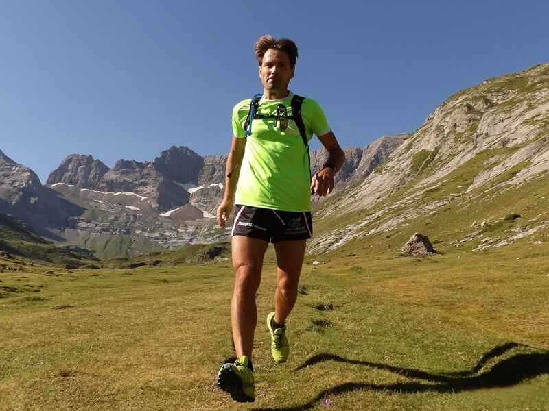 Coureur en montagne sur une prairie verdoyante avec des sommets en arrière-plan