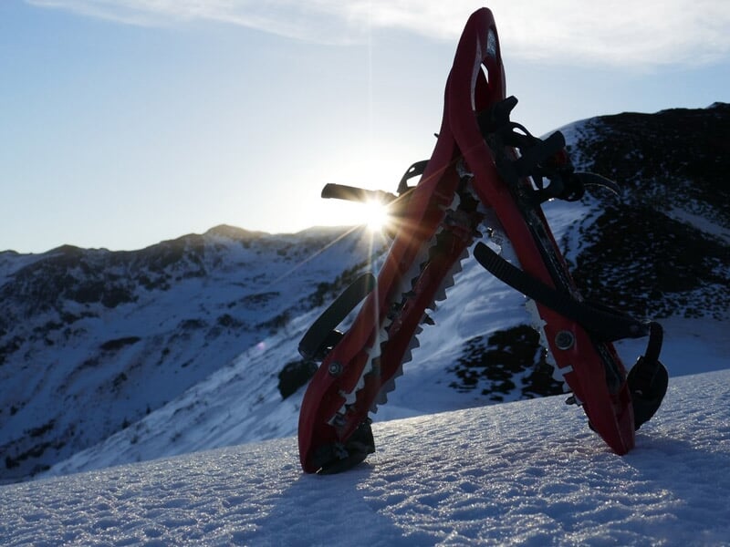 Raquettes à neige rouges posées sur la neige avec le soleil se levant derrière des montagnes.