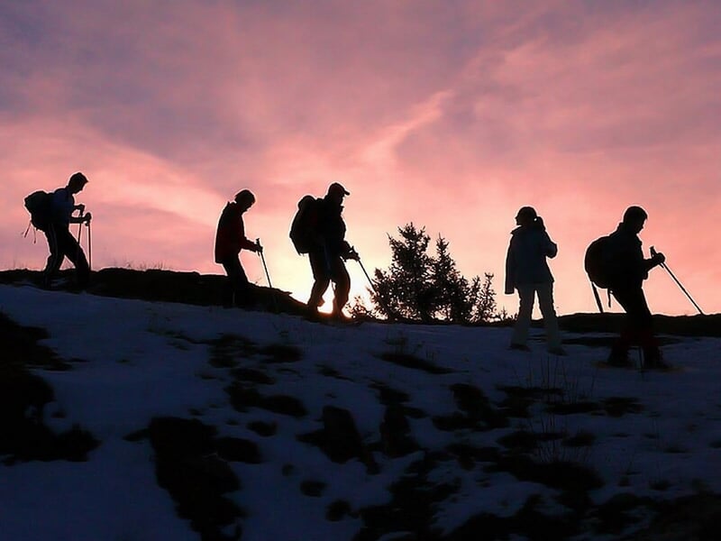 Groupe de randonneurs en silhouette marchant sur un sentier enneigé au coucher du soleil.