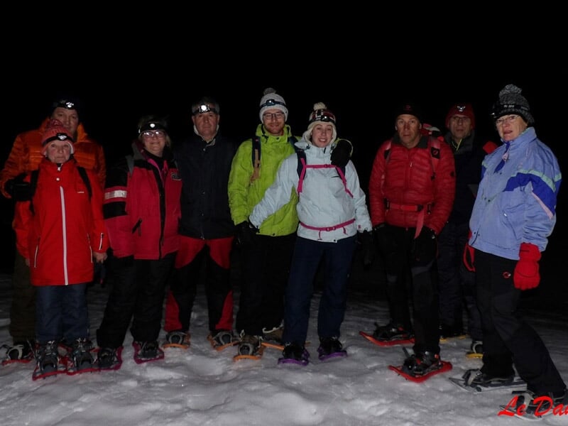 Groupe de personnes en tenue d'hiver posant pour une photo de nuit sur la neige avec des raquettes.
