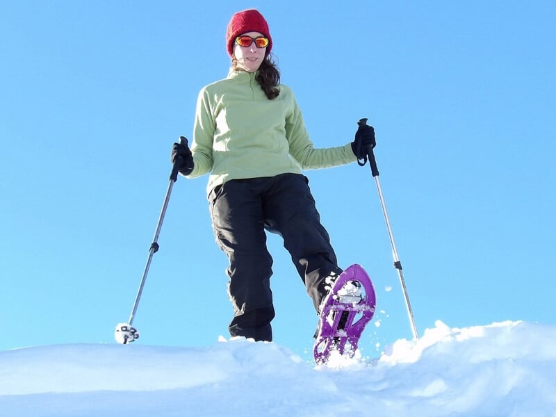 Femme en raquettes à neige debout sur un terrain enneigé sous un ciel bleu clair lumineux.