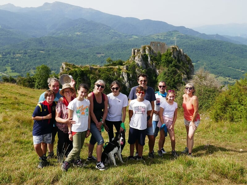 Groupe de randonneurs posant pour une photo en été devant un château en ruines sur une colline verte.