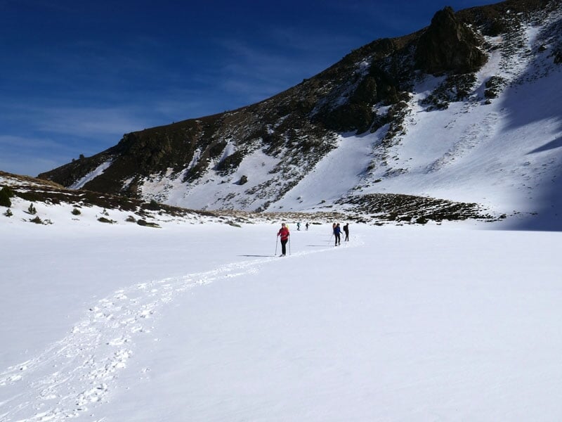 Groupe de randonneurs en raquettes sur un chemin enneigé avec des montagnes en arrière-plan