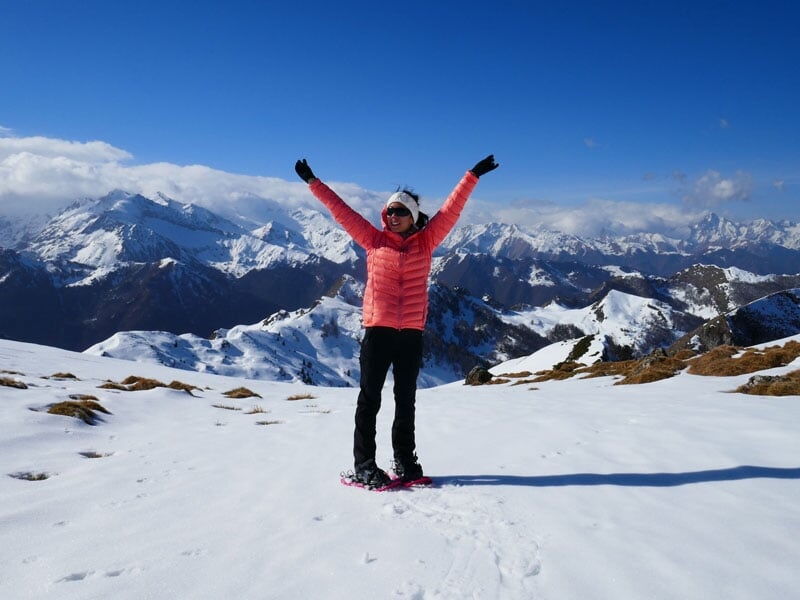 Personne souriante en raquettes debout sur une colline enneigée avec des montagnes enneigées à l'horizon