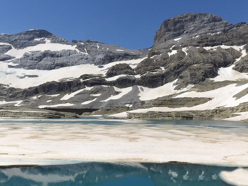 Lac de montagne gelé entouré de sommets enneigés.