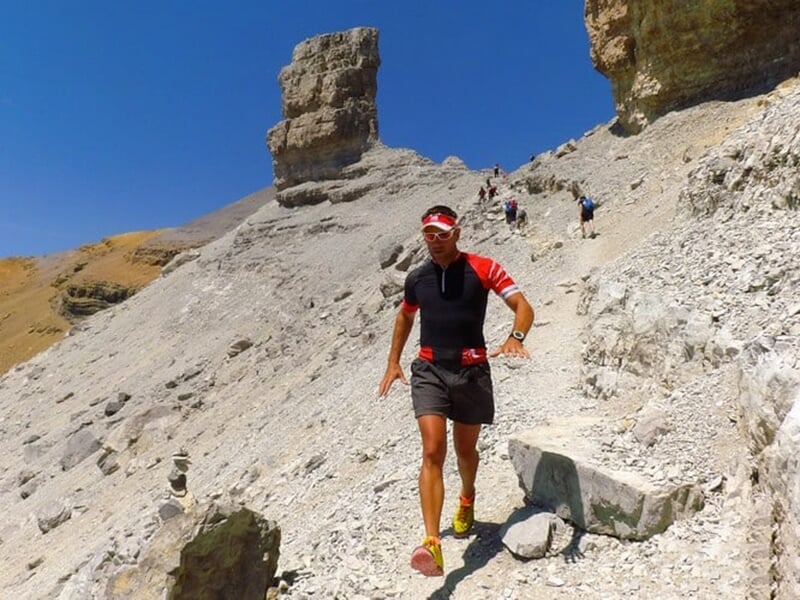 Coureur dévalant un sentier rocheux dans un paysage aride et escarpé.