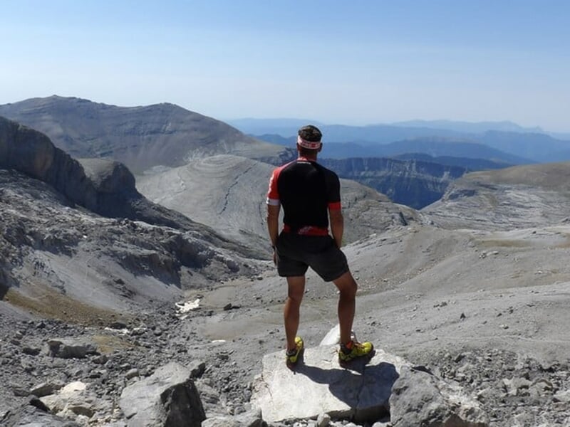 Homme debout sur une crête rocheuse, observant un paysage montagneux.