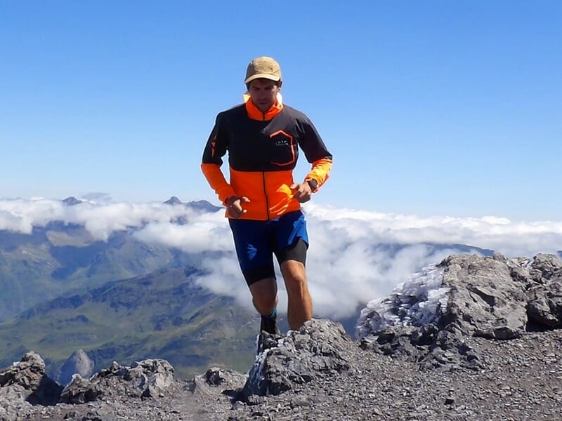 Coureur sur un sommet rocheux avec une vue panoramique sur les montagnes et les nuages.