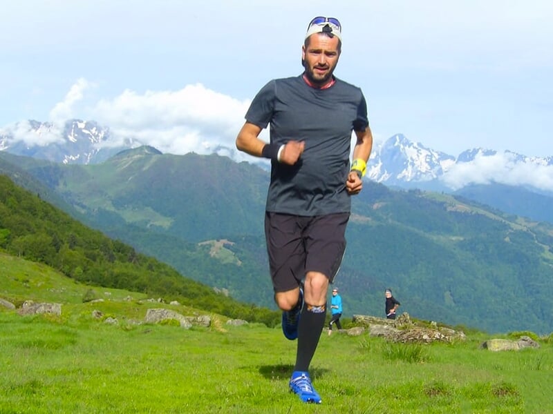 Homme courant sur un sentier de montagne avec des montagnes enneigées en arrière-plan.