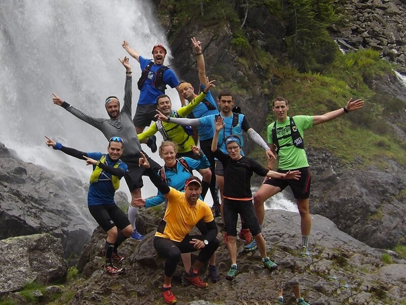 Groupe de coureurs posant joyeusement devant une cascade au milieu de la nature.