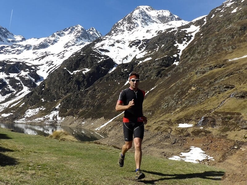 Homme courant près d'un lac entouré de montagnes enneigées.
