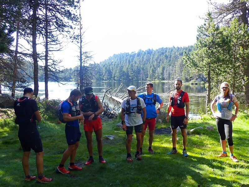 Groupe de coureurs discutant près d'un lac entouré d'une forêt.