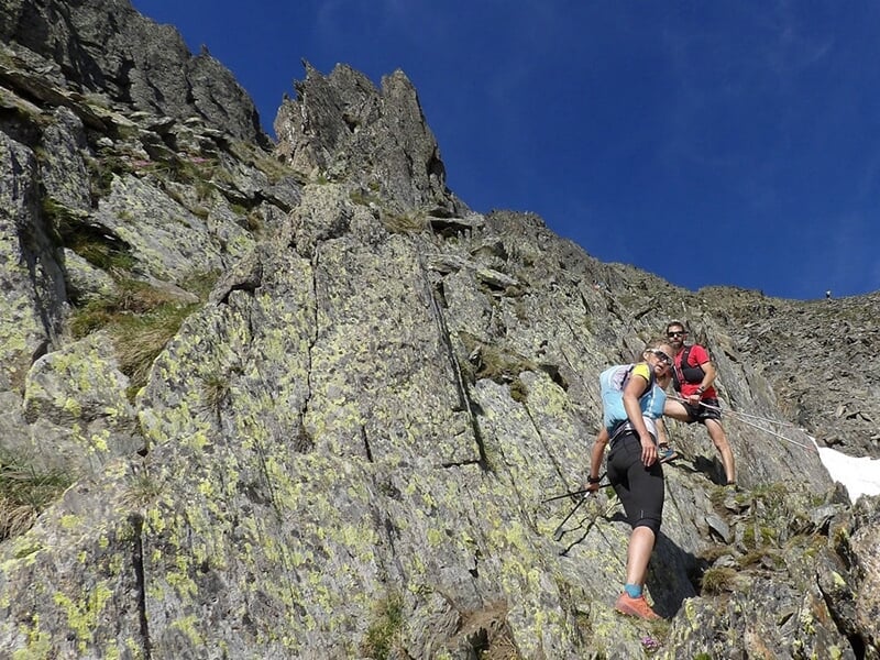 Deux personnes grimpant une paroi rocheuse escarpée sous un ciel bleu.