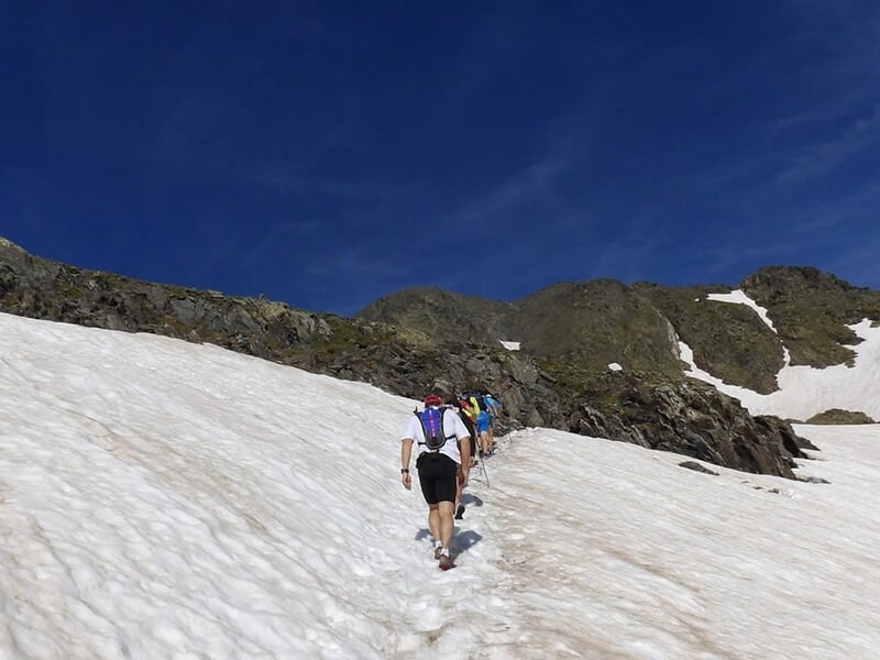 Coureur montant un sentier rocheux avec des lacs alpins et des montagnes à l'arrière-plan.