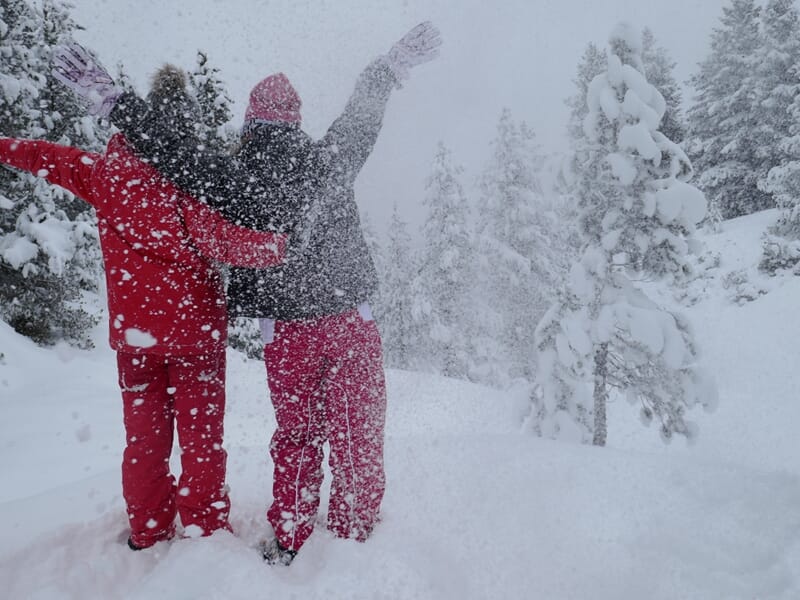 Deux personnes en tenue rouge et grise avec des raquettes à neige dans un paysage enneigé et arbres couverts de neige.