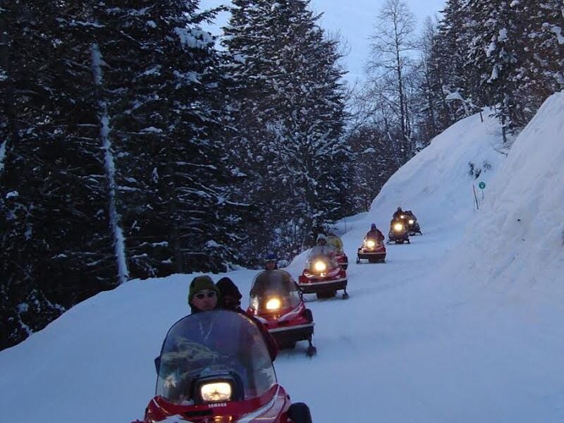 Groupe de motoneiges rouges roulant sur un sentier enneigé entouré d'arbres couverts de neige.