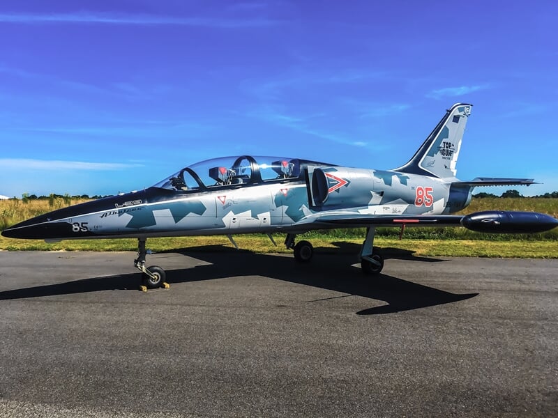 L-39 Albatros stationné sur piste, livrée camouflage gris, ciel bleu en arrière-plan.