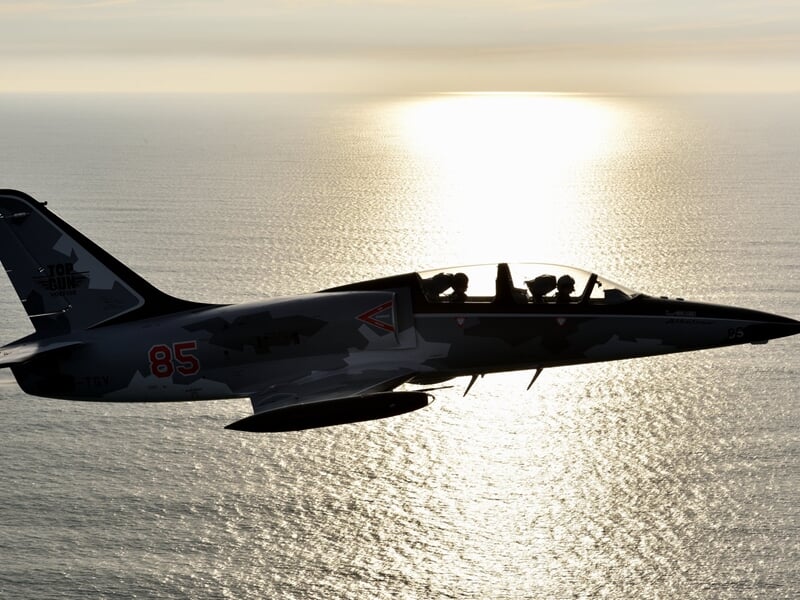 Avion de chasse en silhouette noire volant au coucher du soleil au-dessus de la mer.