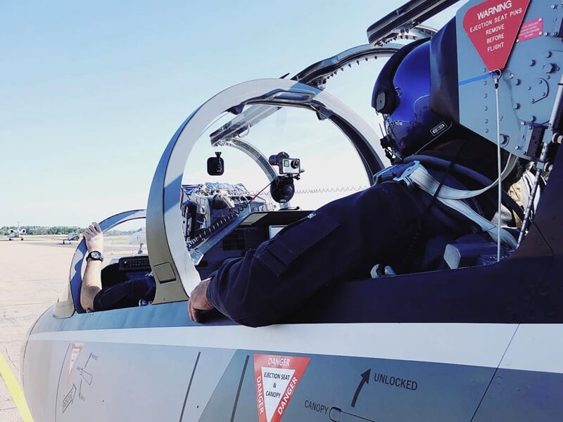 Pilote en combinaison et casque assis dans le cockpit d'un avion de chasse prêt au décollage.