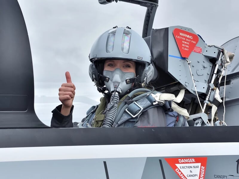 Pilote souriante en combinaison et casque dans le cockpit d'un avion de chasse, pouce levé.