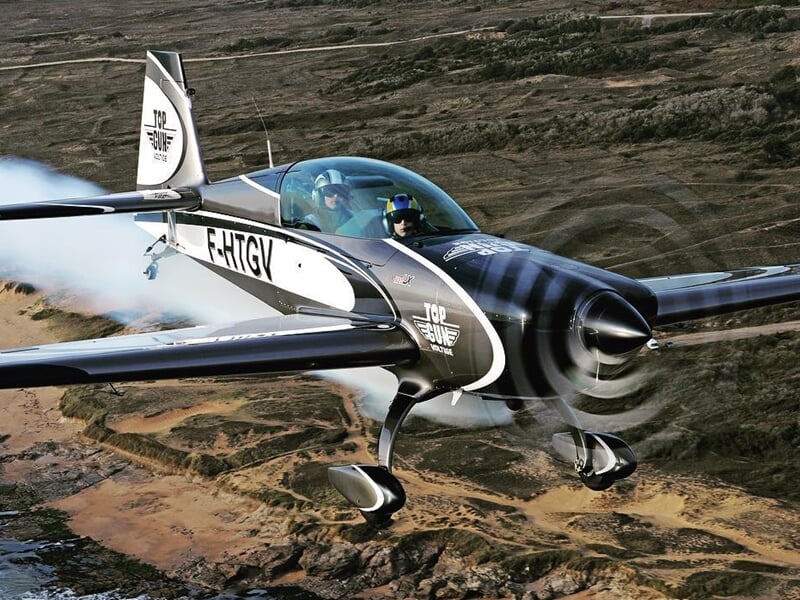 Avion de voltige noir et blanc avec hélice en rotation volant au-dessus d'un paysage désertique.