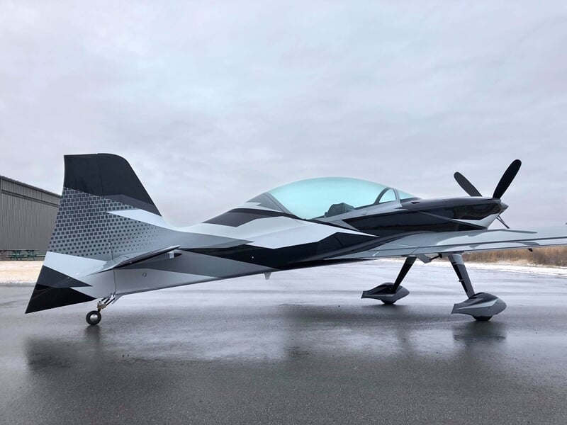 Petit avion de voltige noir et blanc vu de côté sur une piste d'aéroport.
