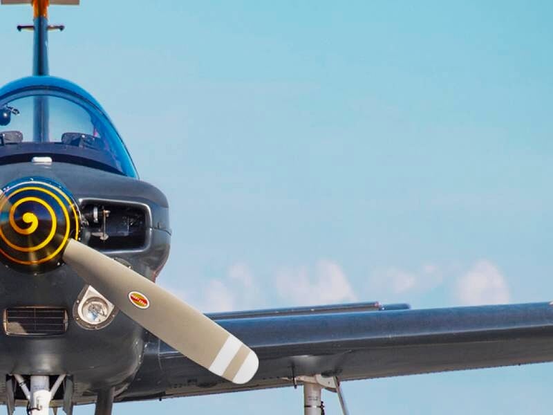 Avion léger bleu avec hélice en rotation volant dans un ciel clair au-dessus d'un paysage sec.