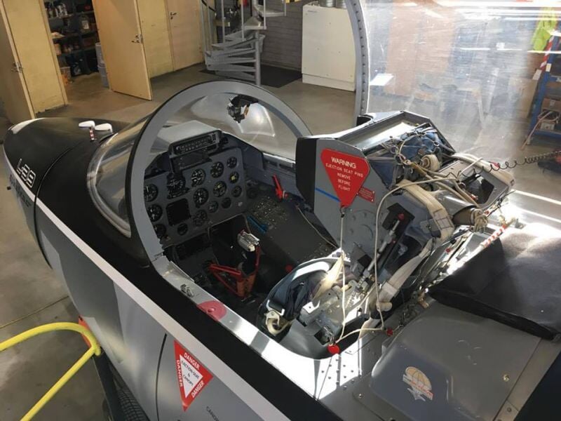 Cockpit d'un avion de chasse avec tableau de bord et commandes visibles dans un hangar d'aérodrome.