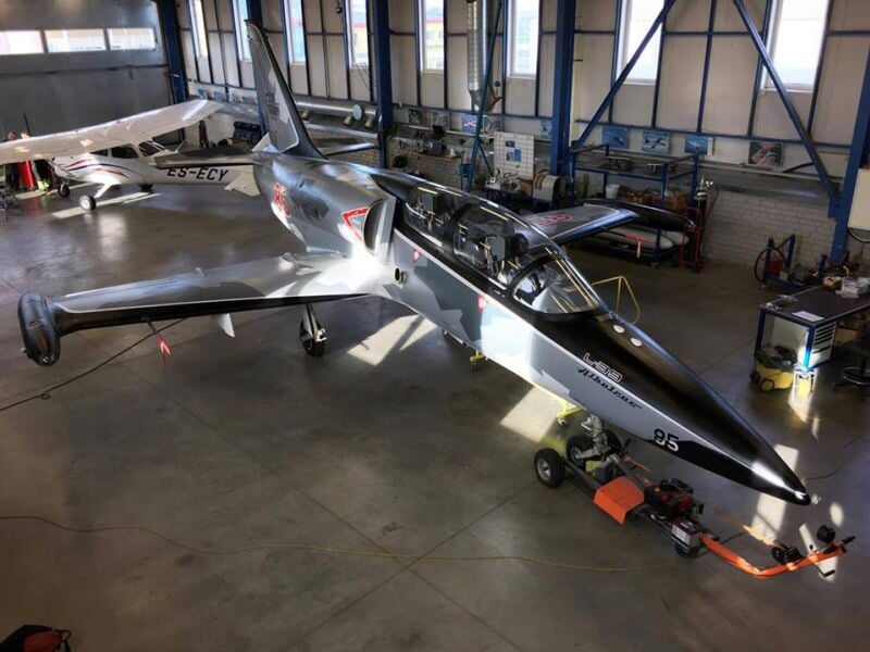 Avion de chasse gris avec camouflage noir et blanc stationné dans un hangar d'aérodrome.