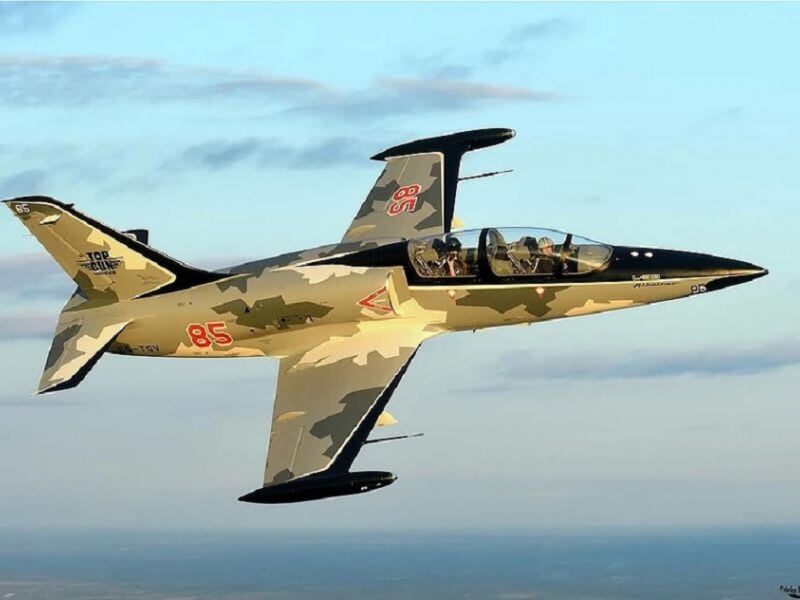 Avion de chasse en vol avec camouflage beige et noir, vu de côté dans un ciel clair.