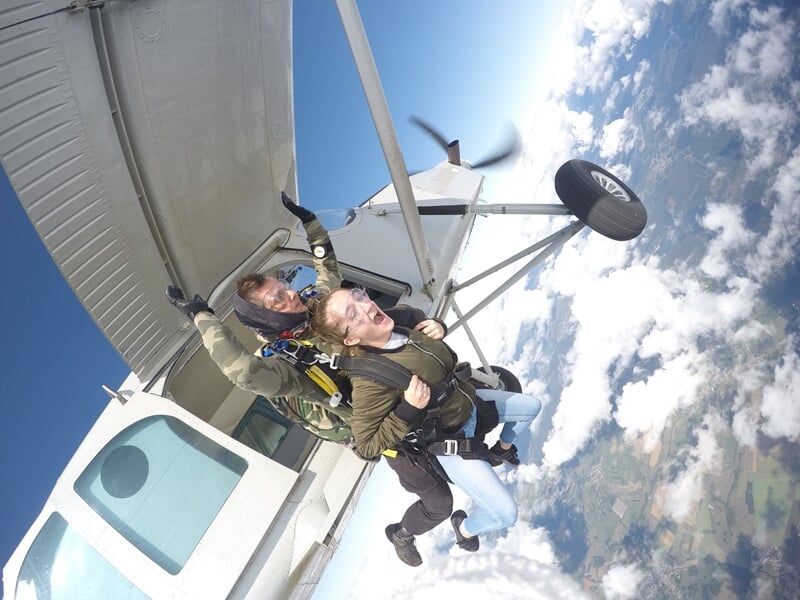 Deux personnes effectuent un saut en parachute en tandem depuis un avion blanc en plein ciel bleu clair.