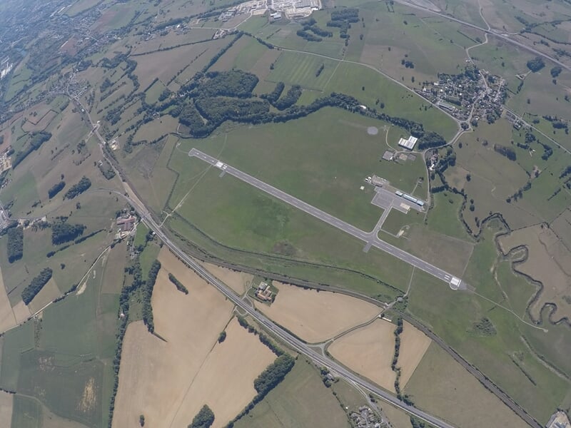 Vue aérienne d'un aérodrome entouré de champs verts et de routes, prise lors d'un saut en parachute.