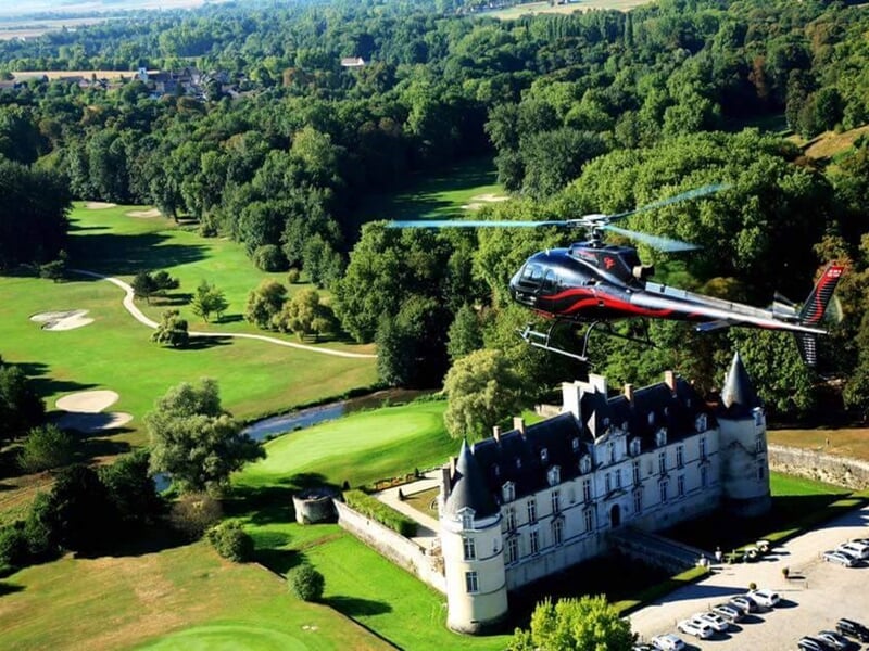 Hélicoptère noir survolant un grand château avec un parc et un terrain de golf verdoyant.