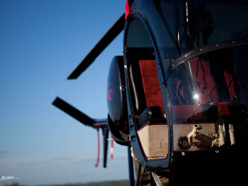 Gros plan sur l'avant d'un hélicoptère noir avec reflet du ciel bleu et pale en mouvement.