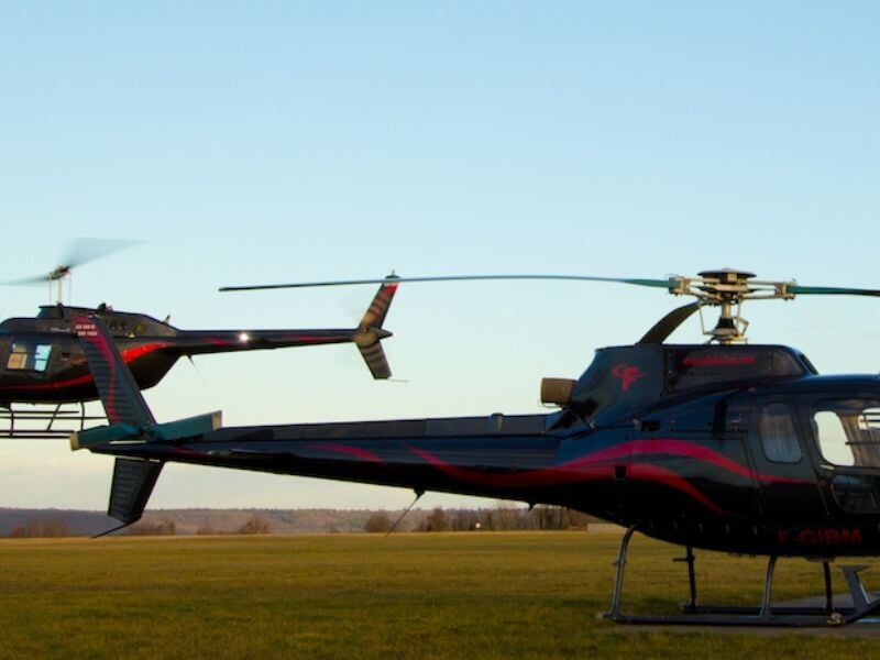 Deux hélicoptères noirs avec motifs rouges stationnés sur un terrain herbeux au coucher du soleil.
