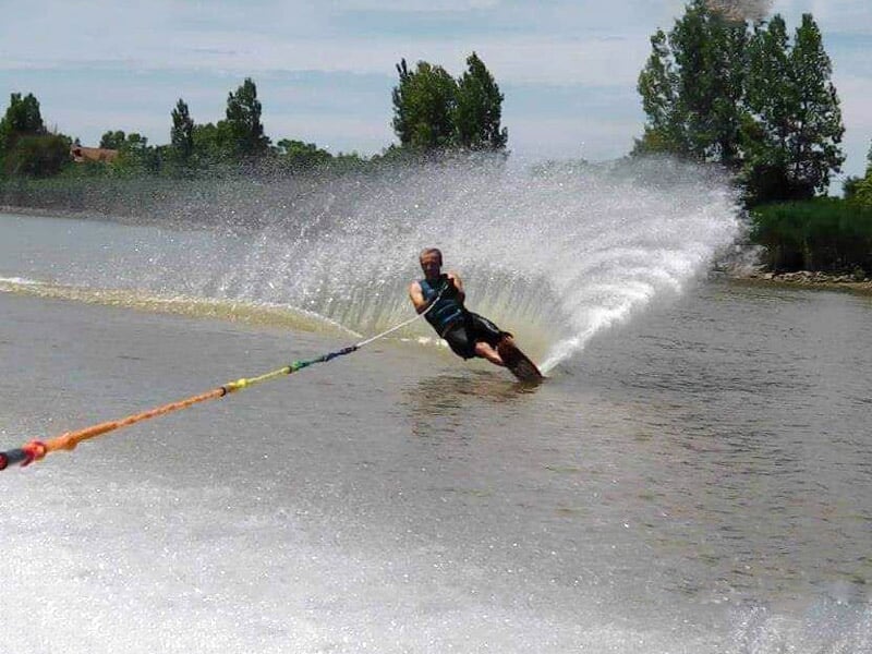 Skieur nautique en action sur un lac, créant une grande gerbe d'eau en virage serré.