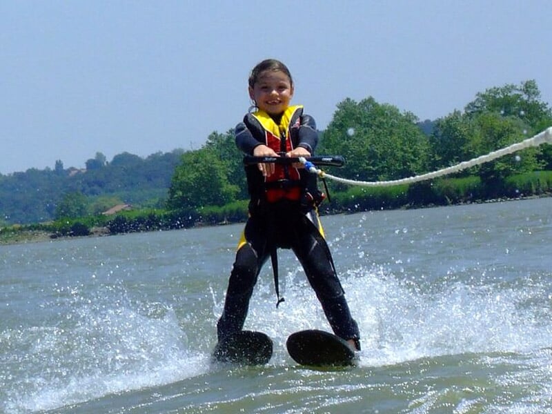 Enfant souriant en tenue de ski nautique, glissant sur l'eau avec un gilet de sauvetage.