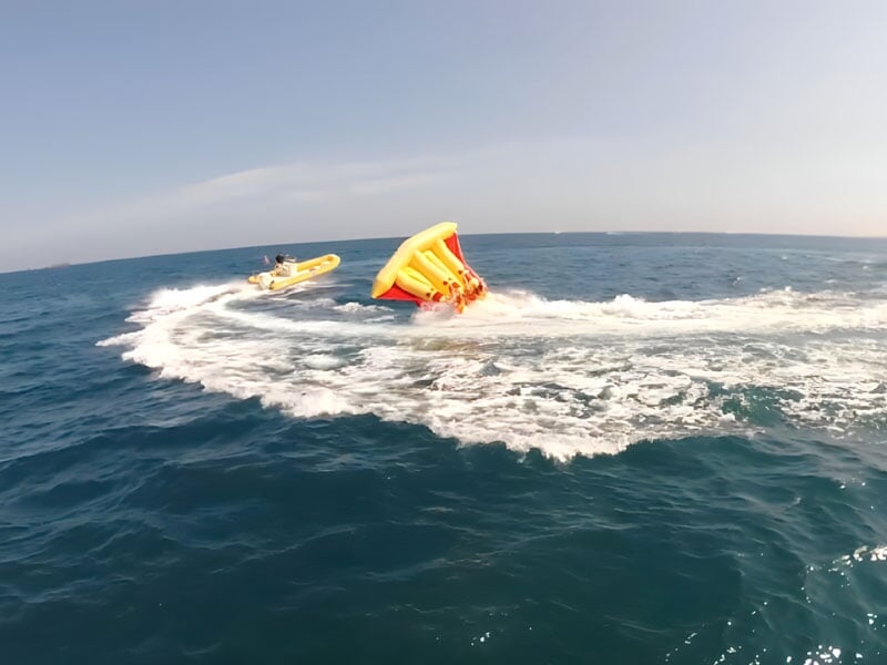 Un bateau pneumatique tractant une bouée gonflable jaune renversée dans l'océan, créant des éclaboussures d'eau sous un ciel clair.