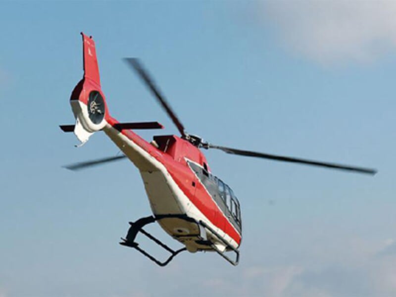 Hélicoptère rouge et blanc en vol dans un ciel bleu clair avec ses pales en rotation rapide.