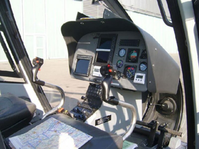 Cockpit d'hélicoptère avec tableau de bord, commandes et une carte posée sur le siège passager.