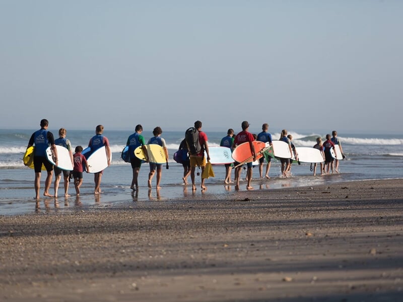 Plusieurs surfeurs marchant vers l'océan avec leurs planches sous le bras sur une plage de sable.