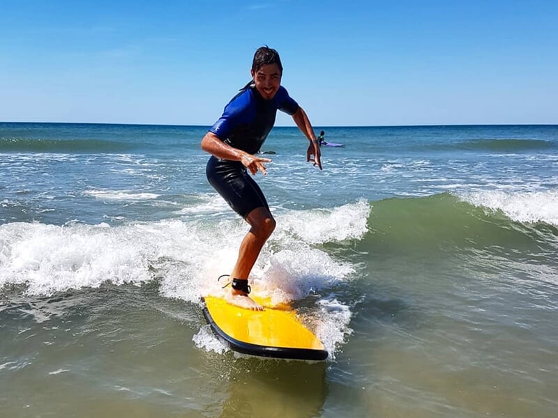 Surfeur debout sur une planche jaune glissant sur une petite vague dans l'océan sous un ciel clair.