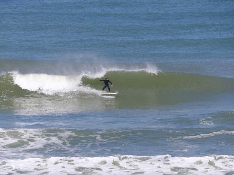 Surfeur solitaire sur une planche blanche, glissant sur une grande vague dans l'océan à La Palmyre.