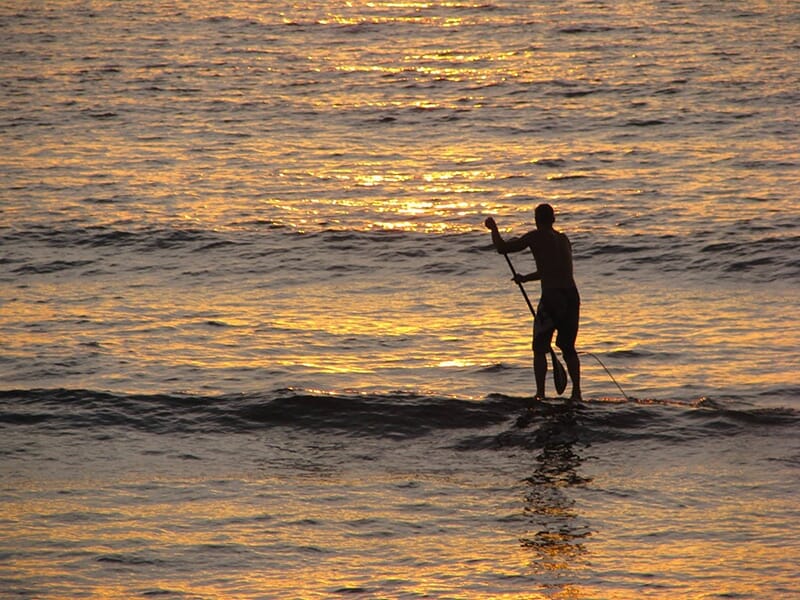 Un surfeur en paddle prend une vague au crépuscule sur l'océan Atlantique